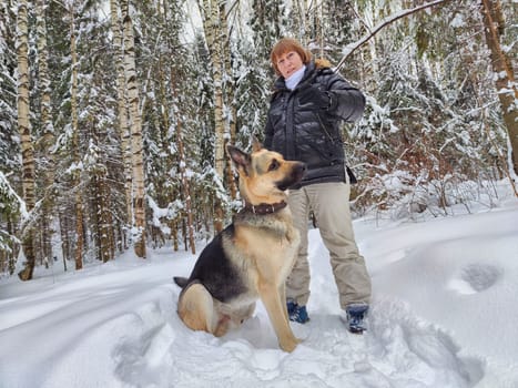 Adult girl, shepherd dog and training in a winter forest. Middle aged woman and big shepherd dog on nature in cold day. Friendship, love, communication, fun