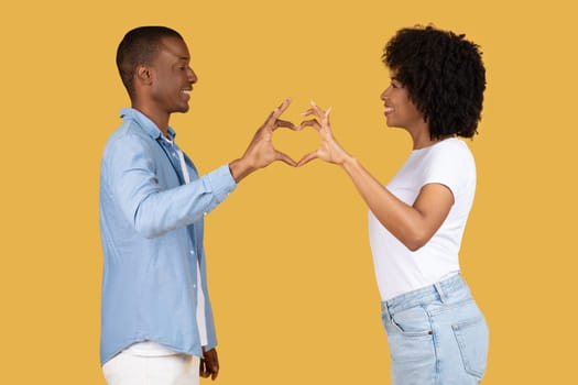 Side profile of a smiling African American couple forming a heart shape with their hands together