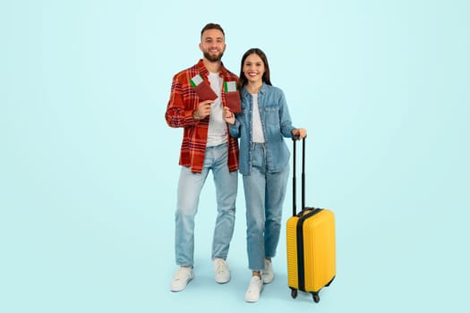 Cheerful caucasian travelers couple standing with tickets and suitcase, studio