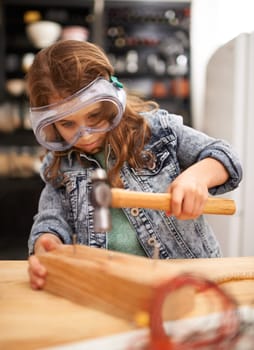 Chilld, construction and hammer a nail in workshop, play and game in kitchen of home. Female person, girl and safety glasses or tool for wood project or hobby, carpentry and remodeling or manufacture