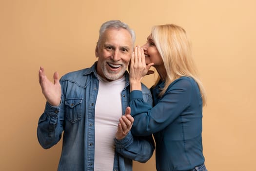 Mature woman sharing secret with her husband, beige background