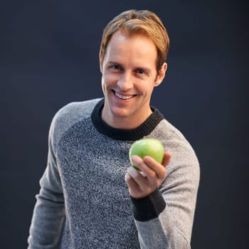 Man, apple and smile in studio portrait with choice for detox, diet or health by dark background. Person, model and happy with green fruit with pride for decision, vegan nutrition and organic snack.