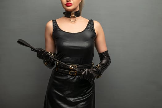 Beautiful dominant brunette mistress woman in latex dress and gloves posing with riding crop