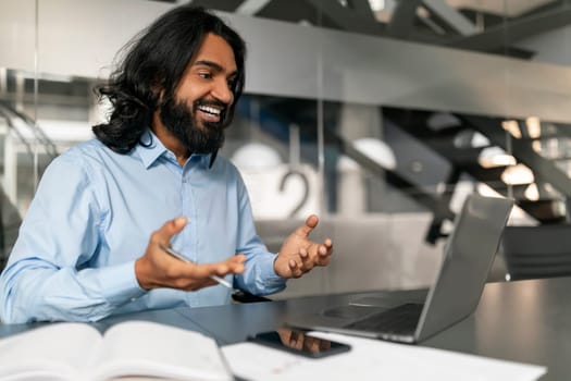 Professional man in a blue shirt working from a modern office space with a laptop, expressing joy and satisfaction