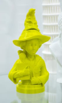 Abstract art object printed on 3D printer. Colored yellow creative model girl in hat printed on 3D printer from molten ABS PLA plastic filament. Object printed FDM printer. Additive modern technology