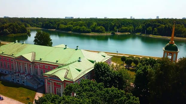 Top view of historic building by river with forest. Creative. Beautiful historical suburb with tourists on riverbank. Picturesque estate on river bank with forest on sunny summer day