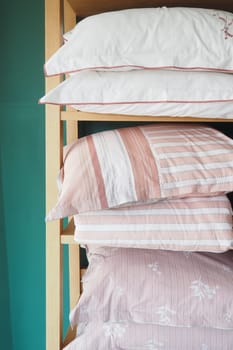 Pillows stacked on wood shelf in bedroom with linens