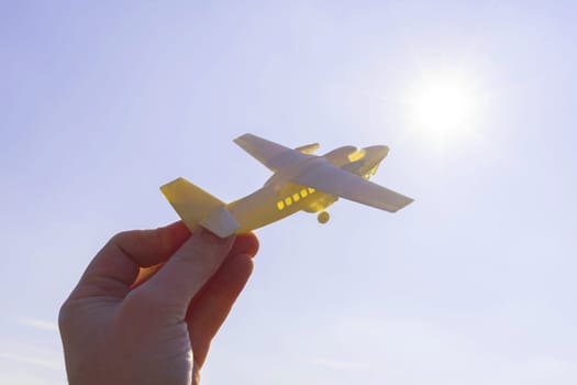 close up photo of male hand holding toy airplane against blue sky.