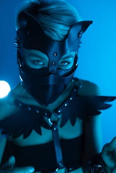 portrait of a hot sexy girl in a leather cat mask and muzzled in bdsm handcuffs on neon blue light