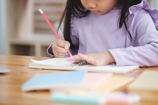 A young girl is writing with a red pencil on a piece of paper