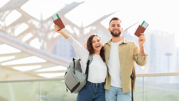 Cheerful young couple ready for trip, raising boarding passes and passports
