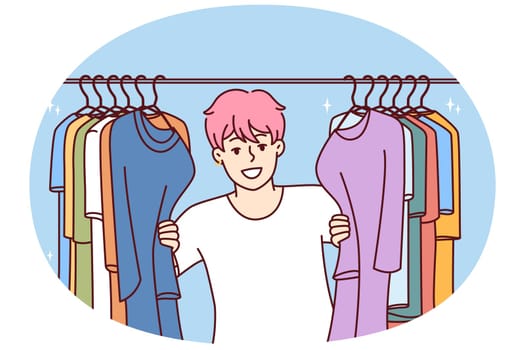 Young Cheerful man in t-shirt smiling peeking out from behind hanger for collection of clothes