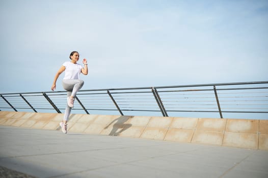 Young woman runner jogger exercising outdoors, running jugging on the city bridge. Female athlete performing morning jog