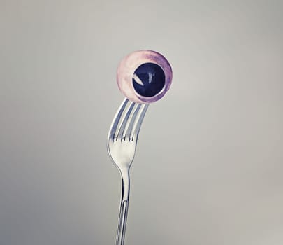 Fork, eyeball and eyes as halloween concept on grey background and weird or crazy art or strange. Horror, odd and abstract of macabre eating in psychology, nightmare and object of discomfort for fear.