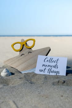 COLLECT MOMENTS NOT THINGS text on paper greeting card on background of funny starfish in glasses summer vacation decor. Sandy beach sun coast. Slowing-down, enjoying the moment, good moments, slow life Holiday concept postcard. Getting away Travel
