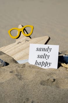 SANDY SALTY HAPPY text on paper greeting card on background of funny starfish in glasses summer vacation decor. Beach sun coast. Slowing-down, enjoying the moment, good moments, slow life Holiday concept postcard. Getting away