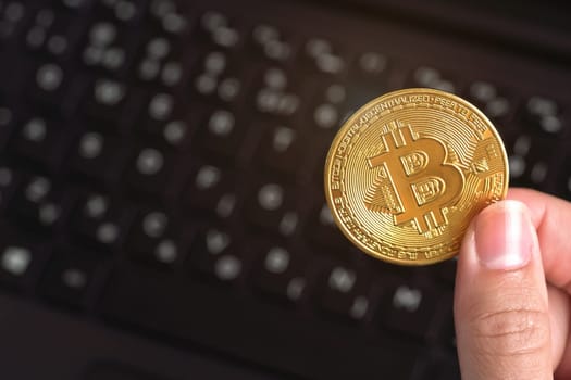 Woman hand holding golden coloured bitcoin coin over black laptop keyboard