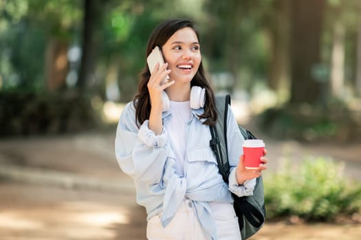 Happy young woman enjoying a lively conversation on her phone while holding a red takeaway coffee cup