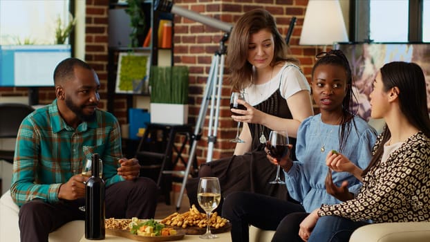 African american man talking asian and caucasian women in apartment living room, gathered together to celebrate festive event. Diverse group of people socializing at home, gossiping about coworkers