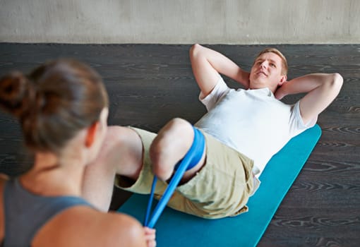 Woman, patient with disability or leg in training, exercise or workout on mat in fitness center. Man, female personal trainer or elastic in stretching, strength or recovery for health and body care.