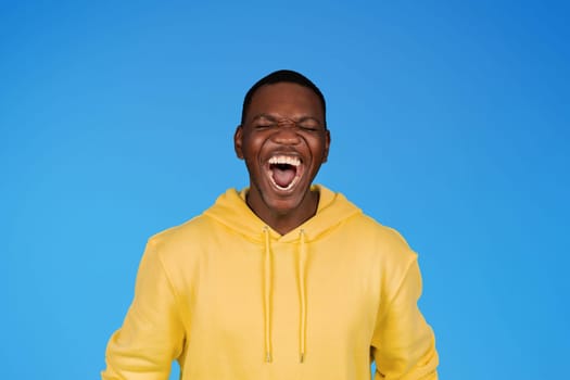 Cheerful laughing excited millennial african american guy in sweatshirt with wide mouth open, enjoy win