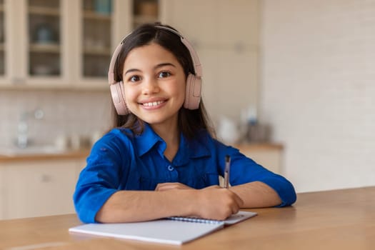 Happy School Girl Learning, Writing in Notebook Wearing Earphones Indoor