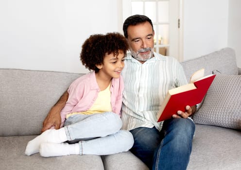 Happy Hispanic Grandson And His Grandfather Read Book At Home