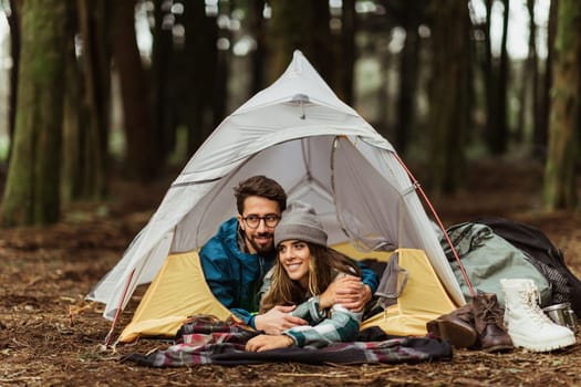 Cheerful young caucasian couple in jackets enjoy travel vacation with tent, sleeping, rest, outdoor. Hiking together, lifestyle, adventure and tourism, camping in wild forest
