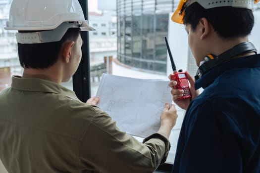 Civil engineers and architects inspecting and working building site with blueprints and holding walkie talkie