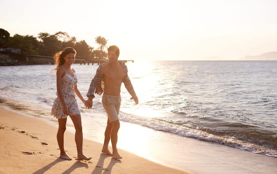 Love, sunset and couple walking at beach for tropical holiday adventure, relax and bonding together. Nature, man and woman on romantic date with ocean, island and evening waves on happy vacation.