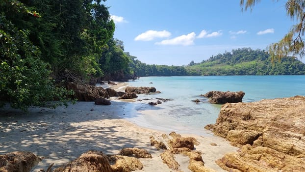 A peaceful beach scene where the waves gently caress the shore, surrounded by a scattering of rocks creating a tranquil atmosphere. Koh Libong Thailand