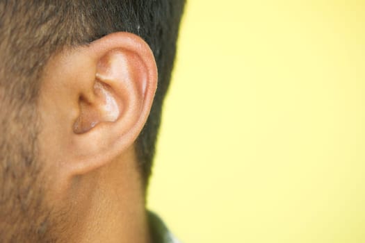 Close up of young man ear with a yellow background.