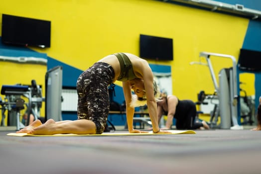 a slender athletic woman in the gym is beautifully engaged in yoga exercises on a mat