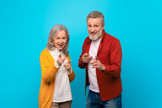 Cheerful mature spouses pointing fingers and smiling at camera, studio