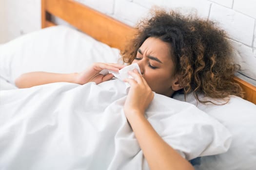 Young sick woman blowing her nose in bed