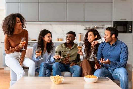 A group of diverse friends enjoy a conversation while holding drinks in a stylish kitchen setting at home