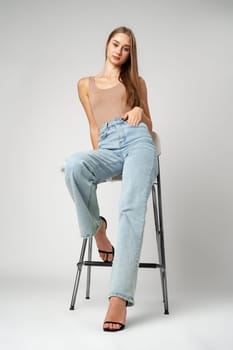 Young Woman Sitting on Stool in High Rise Jeans on gray background