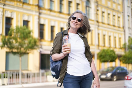 A female pedestrian strolling on the street while holding a beverage in her hand.