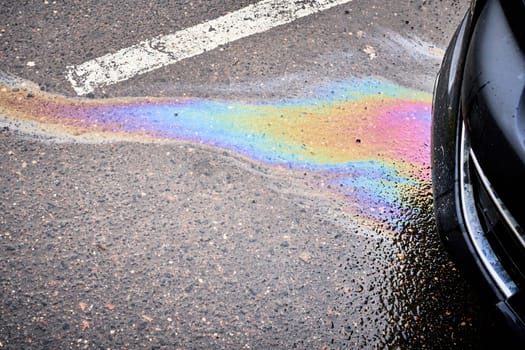 The wet asphalt in a parking lot near a hypermarket is stained with gasoline and oil spill.
