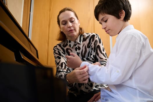 Pianist woman rolls up the sleeves on her student's shirt, prepares him for individual piano lesson
