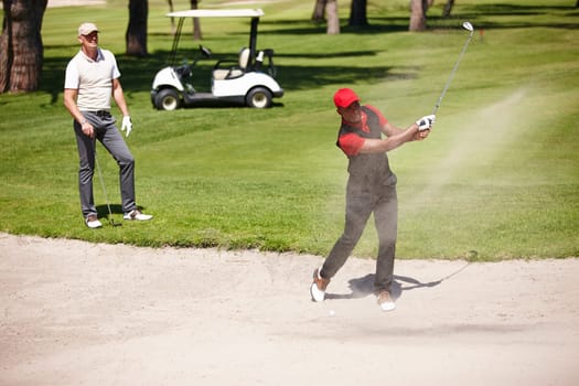 Men, stroke and golf ball in bunker on summer day for sports, health or exercise outdoor in activewear. People, training and playing game of nine holes on natural turf athlete in sand swinging club