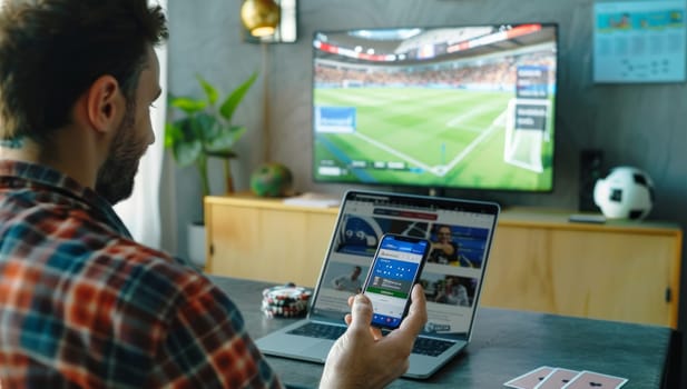 Rear view of a man that watches soccer match on television and bets on the game with betting app on phone