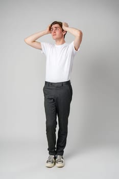 Young Man In White T-Shirt Looking Worried With Hands On Head Against Plain Background