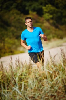 Running, athlete and man, grass and outdoor with energy for practice, exercise and health in nature. Workout, runner and training for marathon, forest and performance of speed for male person