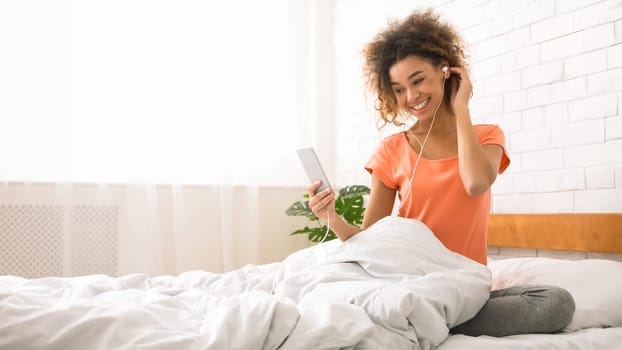 Happy lady listening music with smartphone, sitting in bed
