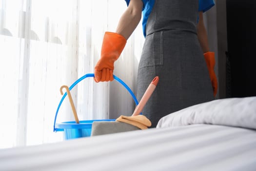 Cropped shot of cleaner woman in rubber gloves holding a basket with cleaning supplies