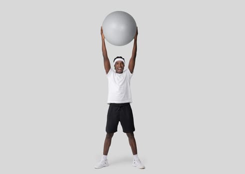 Joyful man lifting exercise ball above his head