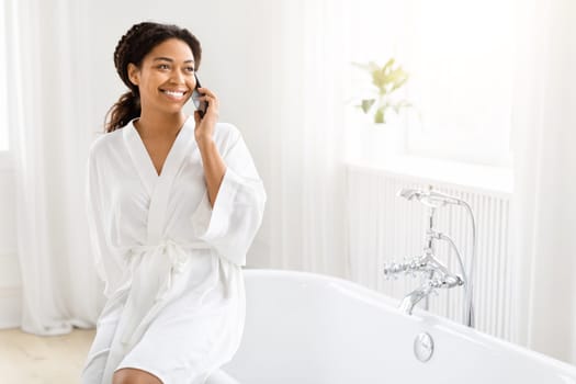 Happy woman talking on phone while sitting on tub