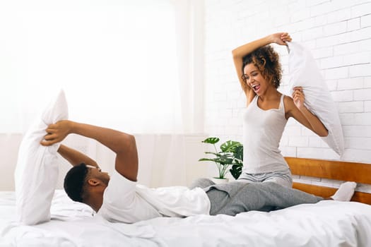 Cheerful loving couple is fighting by pillows in bed.