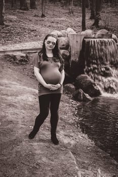 Pregnant girl in the park by the waterfall wearing sunglasses monochrome photo